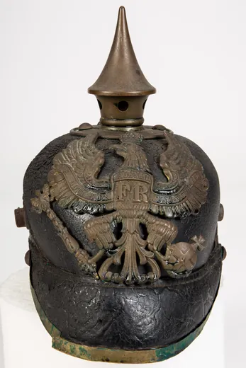 Casque à pointe prussien de troupe d'infanterie de ligne, Première Guerre mondiale, vu de face : cuir noir, aigle de laiton au chiffre FR, pointe sur base ronde à quatre rivets, visière bordée de métal