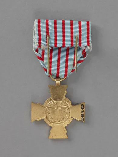 Revers d'une croix du combattant : glaive pointe en bas entouré de rayons, inscription CROIX DU COMBATTANT, ruban bleu horizon à raies rouges monté sur une épingle double