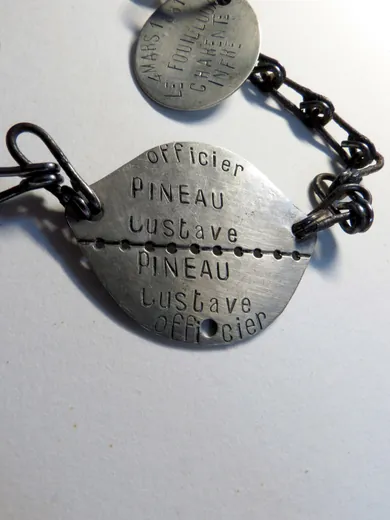 Plaque sécable de l'officier Gustave Pineau, avec son nom répété de part et d'autre de la ligne de rupture, et petite plaque ovale portant sa date et son lieu de naissance
